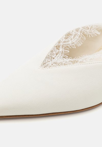 Bailarina de tela blanca con punta afilada, que presenta un diseño de recortes de encaje a lo largo del borde superior. Textura suave y suela de color claro.
