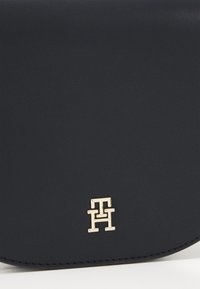 Námořnická syntetická kožená kabelka s texturovaným povrchem a zlatými detaily s logem. Zakřivený tvar se šitými okraji.