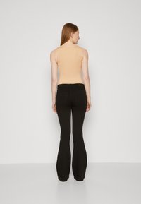 Nude sleeveless top paired with black flared pants. The top has a smooth texture, while the pants feature standard pockets and a fitted waist.
