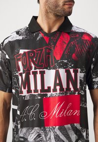 Czarna koszulka polo z krótkim rękawem, zdobiona wyraźnym, teksturowanym nadrukiem z czerwonymi i białymi literami, na których widnieje napis "FORZA MILAN" oraz "A.C. Milan".