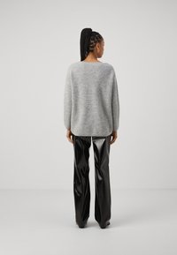 Grau gestrickter Pullover mit lockerer Passform, rundem Ausschnitt und geripptem Textur, kombiniert mit glänzenden schwarzen weit geschnittenen Hosen.