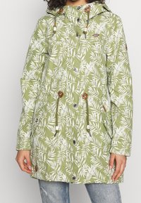 Grön, bladmönstrad knälång jacka med huva, dragsko i midjan, tryckknappar och två framfickor. Tillverkad av lättviktsmaterial.