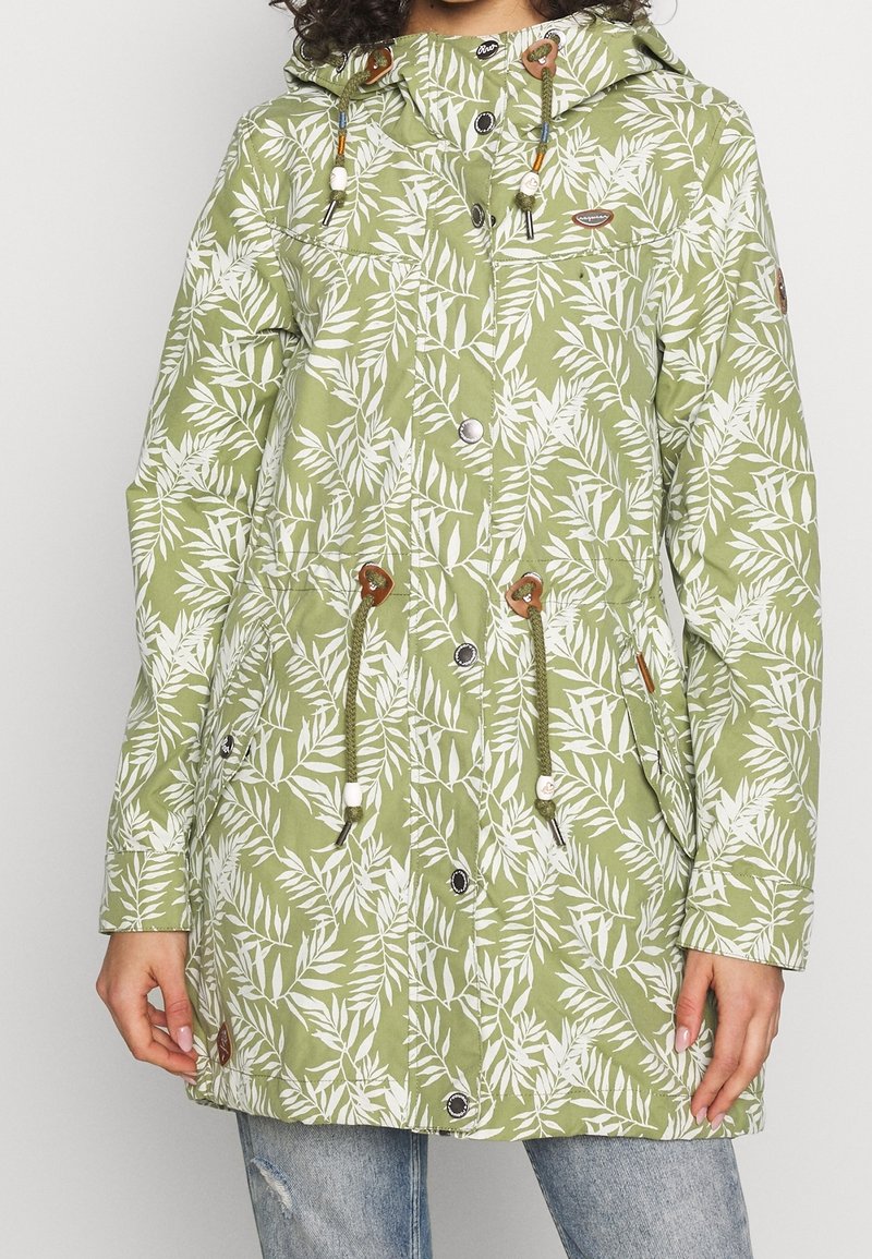 Grön, bladmönstrad knälång jacka med huva, dragsko i midjan, tryckknappar och två framfickor. Tillverkad av lättviktsmaterial.