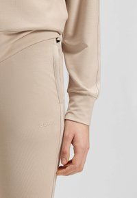 Beige actieve kleding top met lange mouwen, met een zachte textuur en subtiele logo-detail. De bijpassende broek heeft een strakke pasvorm en een zijrits.