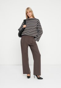 Maglietta a maniche lunghe a righe in marrone e bianco, abbinata a pantaloni larghi a vita alta marroni e scarpe con tacco nere, con una borsa nera.