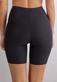 Černé kraťasy s vysokým pasem vyrobené z elastického materiálu, s hladkou texturou a těsným střihem, končící těsně nad kolenem.
