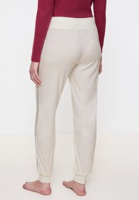 Lichtbeige joggers met een zachte textuur, taps toelopende boorden en zijstrepen. Draag ze met een getailleerde bordeauxrode top, wat een casual pasvorm en stijl laat zien.