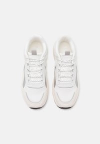 B baskets blanches avec tige synthétique texturée, accents gris, lacets plats et semelles rembourrées. Bout arrondi et finition lisse.