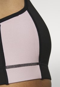 Svart och ljusrosa sport-bh med en slät textur, som har kontrasterande paneler och synliga sömmar längs kanterna.