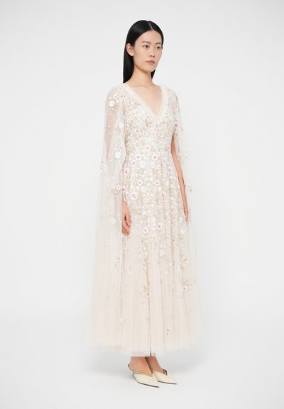 Dlhé krémové šaty s vyšívanými kvetinovými vzormi, priehľadnými rukávmi a výstrihom do V. Textúrovaná tkanina pôsobí jemne a splývavo.