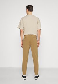 Béžová košile s krátkým rukávem, hnědé kalhoty a černé tenisky. Kalhoty mají zadní kapsy. Hladká látka s příjemným, na míru ušitým střihem.