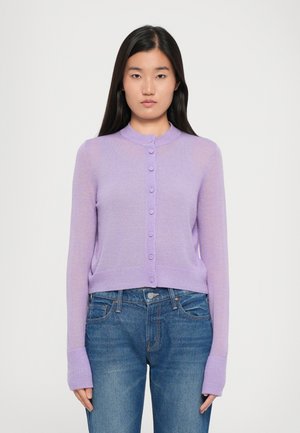 Lys lilla kort cardigan med rund krage, lange ermer og knappefront. Ribbede mansjetter og kant gir tekstur. Båret over denimjeans.
