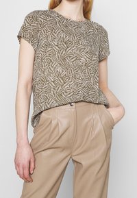 Haut marron à manches courtes avec un motif de feuilles blanches, associé à un pantalon plissé beige, présentant une coupe décontractée et une texture douce.