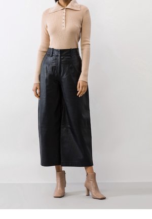 Top in maglia a coste beige con colletto e pattina con bottoni, abbinato a pantaloni larghi neri in pelle a vita alta e stivaletti alla caviglia marrone chiaro.