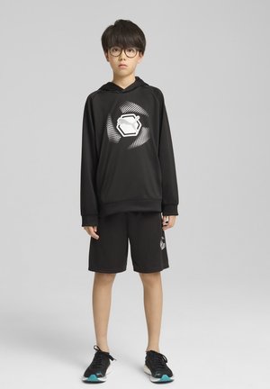 Sudadera deportiva negra con un diseño gráfico blanco y pantalones cortos, fabricada con material ligero. Combinada con zapatillas negras con acentos turquesa.