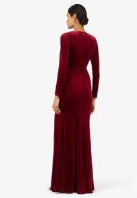 Langärmliges, bodenlanges Kleid aus burgunderrotem Samt, mit einem taillierten Oberteil, das ab der Taille ausläuft, und einem verdeckten Reißverschluss im Rücken.