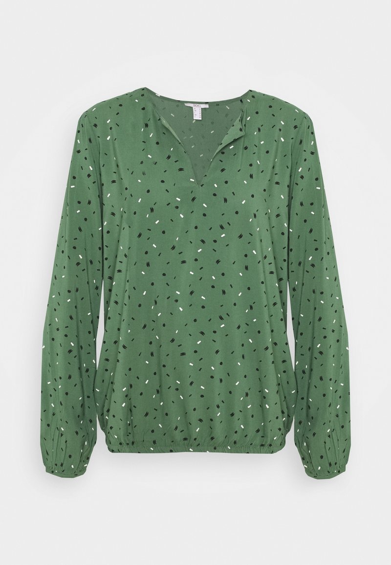 Blouse verte à manches longues avec un décolleté en V, présentant un motif éparpillé de pois noirs et blancs, des poignets froncés et une coupe décontractée.