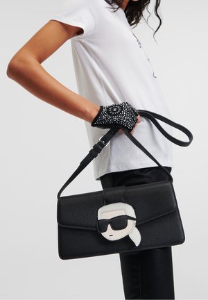 Black textured handbag with a cartoon face design on the front, featuring sunglasses. Includes a detachable strap for carrying.