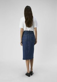 Mørkeblå denim midi-skirt med en tettsittende midje, har to baklommer og en rå kant. Kombinert med en hvit t-skjorte med kort erm.