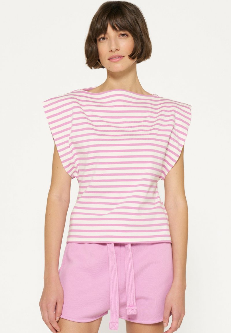 Camiseta de rayas en rosa y blanco, con amplias solapas en los hombros y un escote redondeado. Combinada con pantalones cortos rosa a juego con cordón.