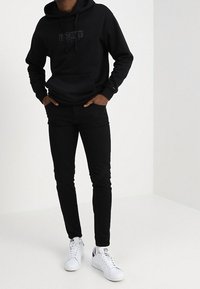 Černá mikina s kapucí s tónovým logem "TOMMY", úzké černé kalhoty a bílé tenisky, s minimalistickým designem a hladkými texturami.
