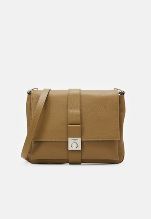 Hellbraune Leder-Crossbody-Tasche mit Frontklappe, mittigem Riemen und quadratischem silbernem Verschluss auf einfachem weißem Hintergrund.