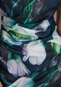 Il tessuto floreale presenta tulipani bianchi e viola su uno sfondo blu scuro con foglie verdi. Texture liscia, design aderente con dettagli arricciati.