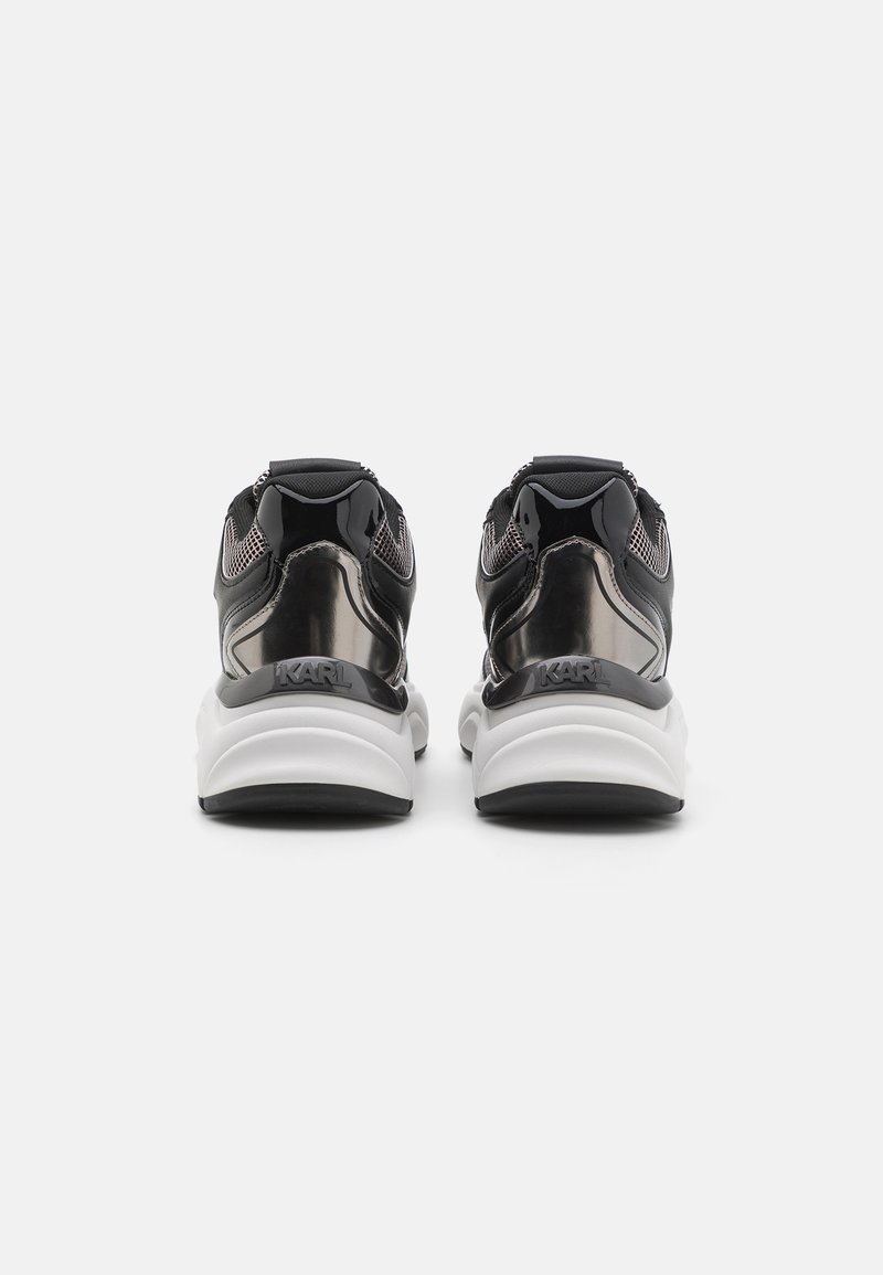 Zwart-witte sneakers met glanzende accenten, gaaspanelen en een gevoerde kraag. Opvallend logo en dikke, gevoerde zool voor comfort.