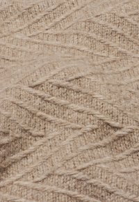 Beige gestrickter Stoff mit einem strukturierten, welligen Muster. Das Material wirkt weich und dick, mit sichtbaren Fasern und einem warmen, gemütlichen Gefühl.