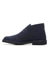 Zapato de ante azul marino con punta redonda, diseño de cordones con dos ojales y suela de goma negra. Presenta costuras a lo largo del borde de la suela.