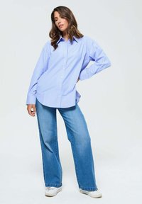 Chemise à boutons rayée bleu et blanche avec manches longues, associée à un jean en denim à jambes larges et des baskets blanches. Tissu au texture lisse.