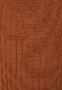 Maglione a coste in arancione ruggine, che presenta un motivo testurizzato con linee verticali. Tessuto morbido con leggera lucentezza, spessore medio.