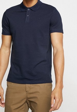 Marineblå polo i blødt bomuld med klassisk krave, to-knaps knapliste og korte ærmer. Enkel og figursyet design.