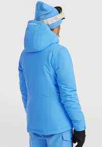Blauwe geïsoleerde skijas met een capuchon, met een gladde textuur en naden. Het merkembleem is zichtbaar op de achterkant in het wit.