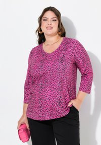 Rosa Leopardenmuster-Oberteil mit V-Ausschnitt, Dreiviertelärmeln und weichem Material, kombiniert mit einer passenden rosa Clutch-Tasche.