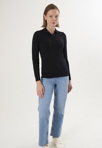 Sort poloshirt med lange ærmer, knaplukning og krave, kombineret med lyseblå jeans med lige ben og hvide sneakers.