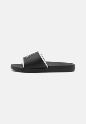 Black slide sandal with a matte finish, featuring a wide strap with white trim and logo detail. Textured black sole for grip.