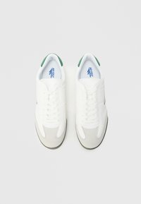 Bijele tenisice sa zelenim akcentima na peti, s glatkom kožnom gornjom stranom, vezicama za vezanje i sivim brušenim slojem na prstu.