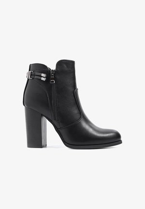Stivale alla caviglia in pelle nera con tacco a blocco alto, zip laterale e doppi cinturini con hardware argentato. Texture liscia, design elegante.