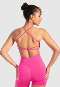 Aansluitende roze sportbeha met een gekruiste bandontwerp en hoge roze shorts met geribbelde tailleband en een gladde textuur.