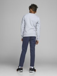 Sudadera de algodón gris, pantalones azul marino y zapatillas negras con acentos naranjas; cabello rizado visible, visto desde la parte de atrás.