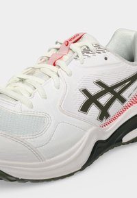 Αθλητικό παπούτσι Asics σε λευκό και μαύρο με λευκά κορδόνια, κόκκινες λεπτομέρειες και υφασμένη σόλα σε απλό φόντο.