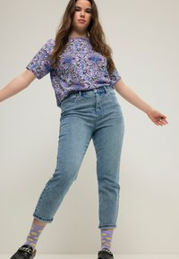 Lyhyet hihais purplekuvioiset paita, korkeavyötäröiset vaaleansiniset farkut ja violetit sukat, joissa on hymyileviä naamoja. Mustat liukuhihnasandaalit täydentävät asun.