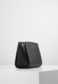 Černá kožená kabelka se strukturovaným tvarem a hladkou texturou. Má zlaté kování a na přední straně je zobrazeno logo.