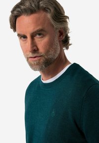 Dunkelblauer Strickpullover mit rundem Halsausschnitt. Verfügt über ein dezentes Logo auf der Brust und eine gerippte Textur um den Kragen.