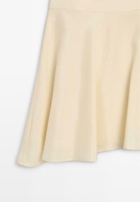 Roomkleurige A-lijn rok van gladde stof met subtiele uitlopende zoom, getoond van midden taille tot zoom tegen een effen achtergrond.