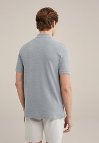 Pelēka polo krekla ar mīkstu tekstūru, īsām piedurknēm un klasisku apkakli. Šūti apakšmalā un sānu šķeltnēs, valkāts ar baltām šortiem.