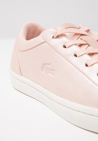 Baskets en cuir rose avec une texture lisse, semelle en caoutchouc blanche et détail subtil de logo en relief. Les lacets sont assortis en rose.