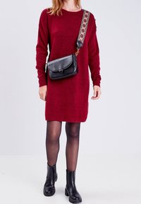 Vestido de punto burdeos con mangas largas, acompañado de un bolso cruzado negro con una correa decorativa y botines.