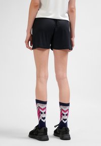 Svarta sportshorts med en slät textur, tillsammans med mönstrade strumpor som har rosa och lila geometriska mönster, samt svarta sportskor.